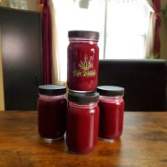 A table with four jars of red juice on it.