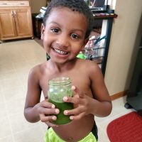 A young boy holding a jar of green juice.