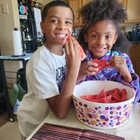 Two children eating watermelon in a kitchen.