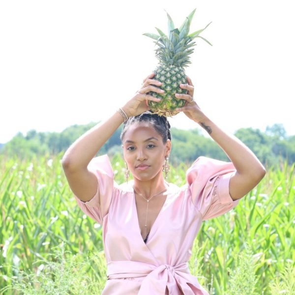 A woman holding up a pineapple in the grass.