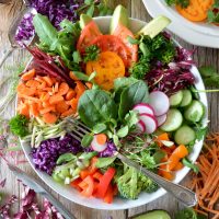 A bowl of salad with vegetables and fork on the side.